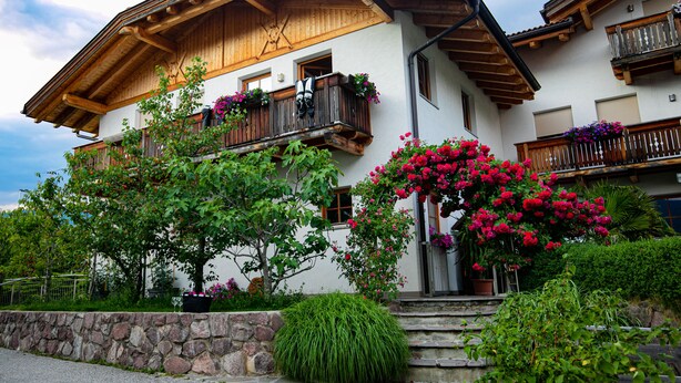 A traditional chalet with wooden balconies, stone steps, and lush greenery. - Ferienwohnung mit Schwimmbad (Schabs)