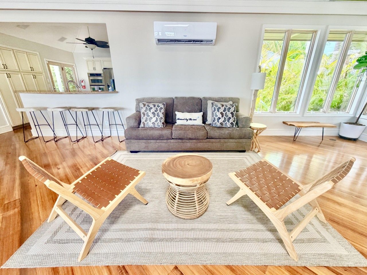 A living room with a sofa, two wooden chairs, a coffee table, and a kitchen in the background.