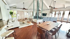 A spacious living area with a wooden dining table, a sofa, and a kitchen in the background.