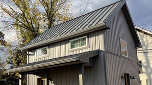 Une maison à deux étages avec un porche couvert, une petite porte d’entrée et une fenêtre.