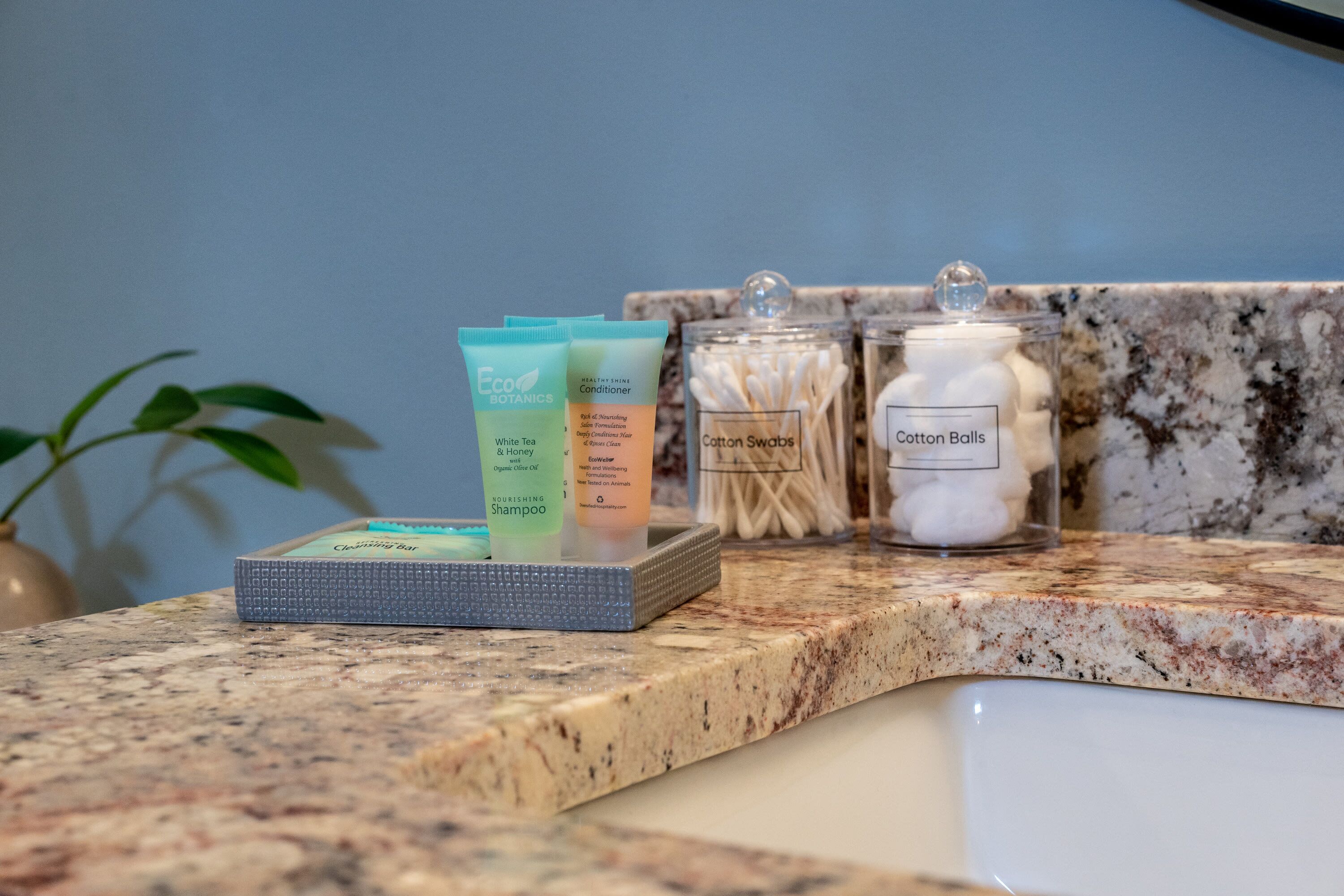 A countertop with toiletries including a cleansing bar, conditioner, and cotton swabs.