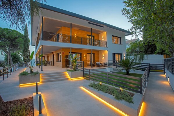 A modern two-story house with a balcony, outdoor seating area, and a well-lit pathway.
