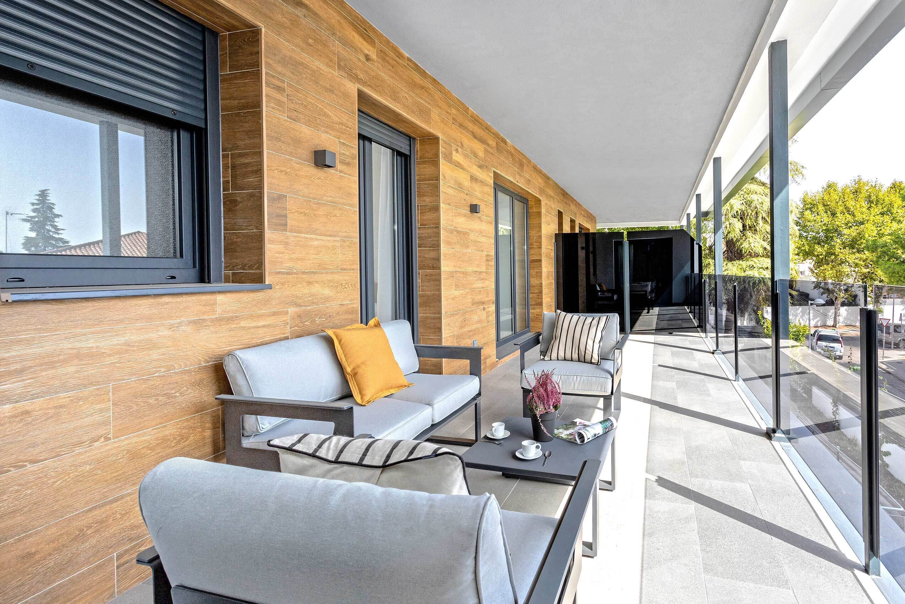 A modern balcony with a wooden wall, a sofa, a coffee table, and a dining area.