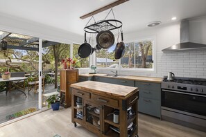 A modern kitchen with a wooden island, hanging pots, and a large window.