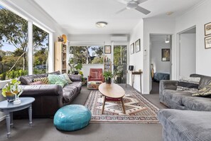 A spacious living area with a leather sofa, a round ottoman, and a coffee table. There are bookshelves and a variety of decorative items.