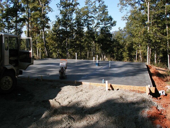 Construction site with a partially paved area surrounded by trees and a stationary vehicle.