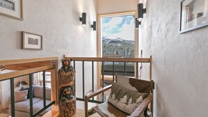 Une pièce avec un escalier en bois, un canapé agrémenté de coussins à motifs, une chaise en bois et une grande fenêtre donnant sur les montagnes.