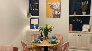 Un coin repas avec une table ronde, des chaises roses et un vase de fleurs.