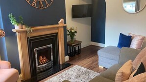 Un salon avec une cheminée, une grande horloge murale, un téléviseur à écran plat et un miroir.