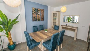 Een eethoek met een houten tafel en blauwe stoelen, een potplant, een kast met glazen deuren en een spiegel aan de muur.
