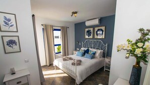 Een slaapkamer met een bed, nachtkastjes, een kaptafel, een raam met gordijnen en wanddecoratie.