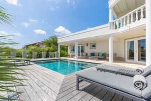 Uma área de piscina com espreguiçadeiras, um deck de madeira e um espaço de estar coberto com vista para a piscina.