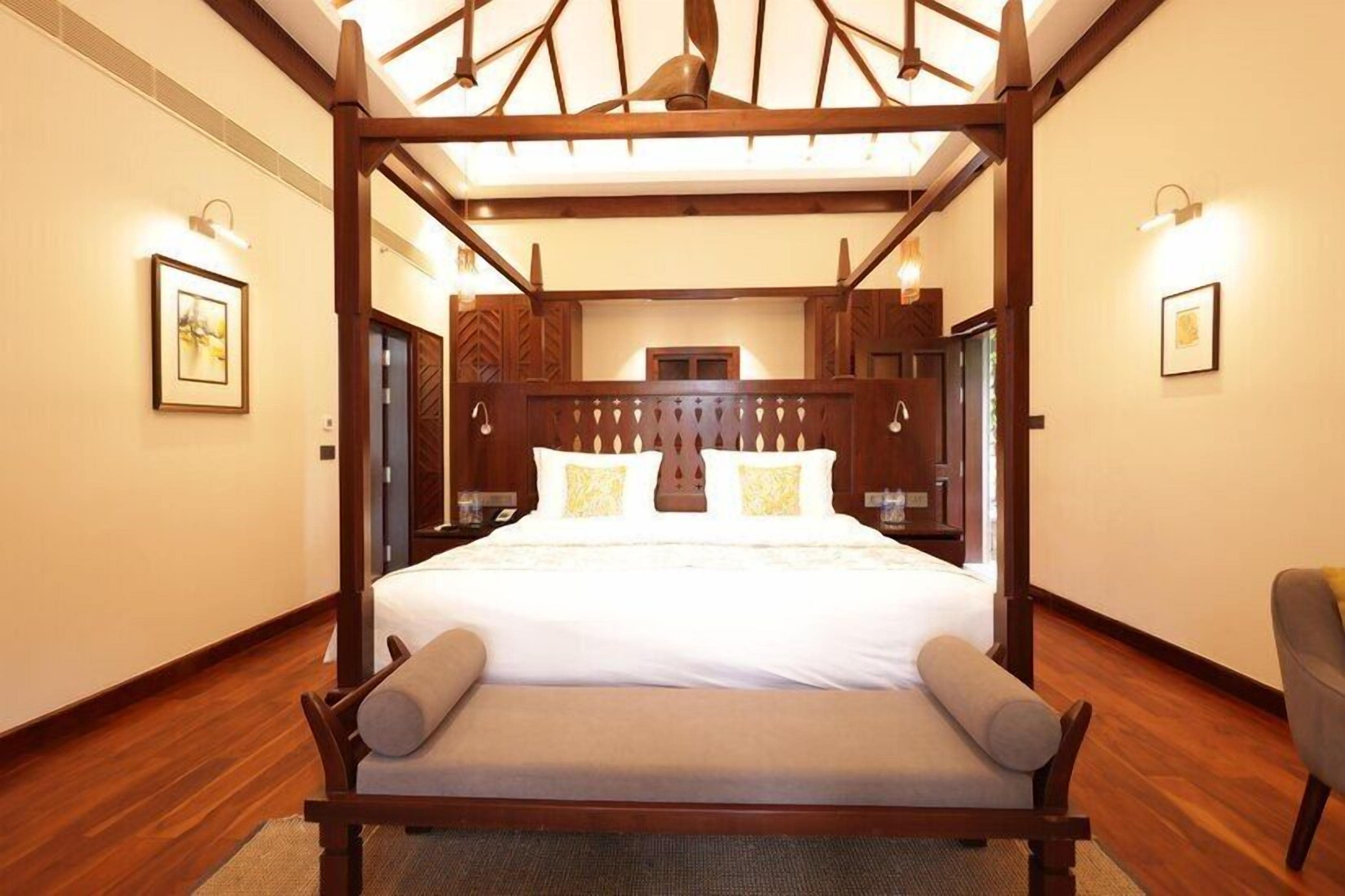 A four-poster bed with a wooden canopy, a bedside table, and a chair.