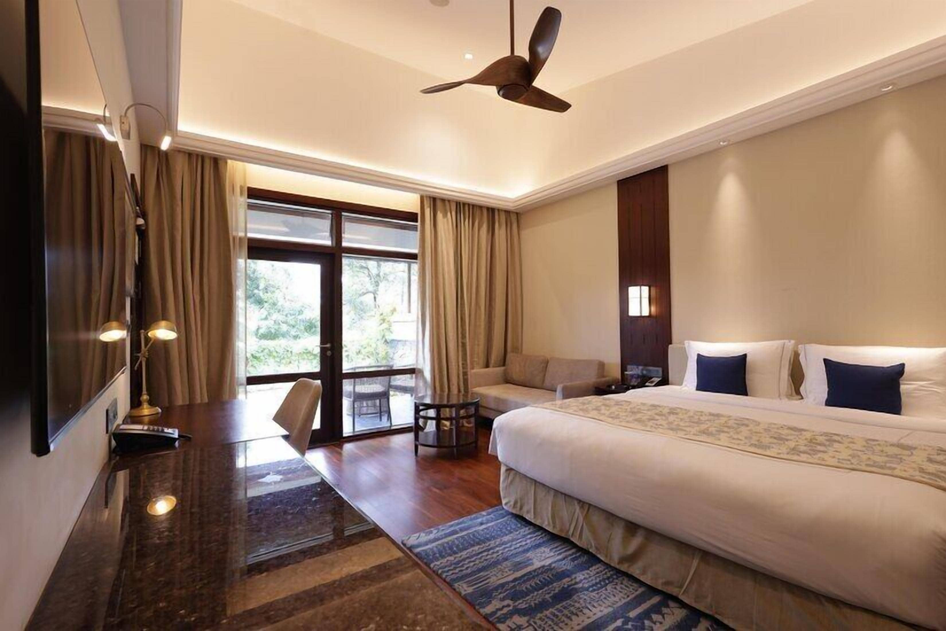 A hotel room with a large bed, a desk, a chair, and a ceiling fan.