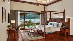 A spacious bedroom with a four-poster bed, a wooden desk, and a view of a lake. - Taj Wayanad Resort & Spa, Kerala (Vythiri)
