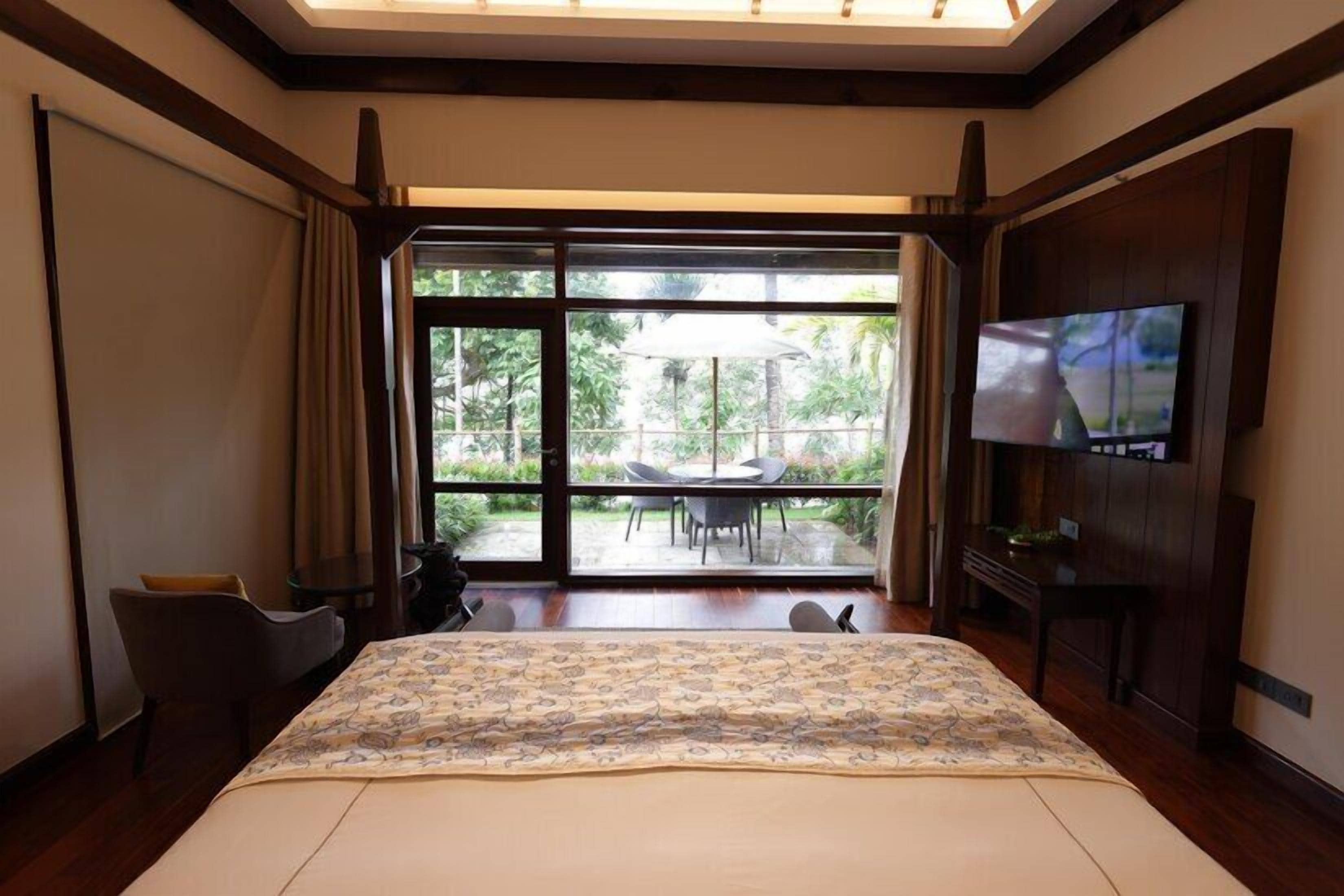 A hotel room with a large bed, a TV, a desk, and a view of the outdoors.