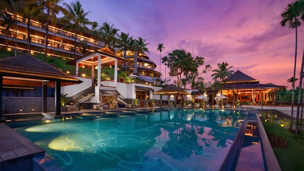 A resort with a large swimming pool, multiple balconies, and palm trees. - Taj Wayanad Resort & Spa, Kerala (Vythiri)