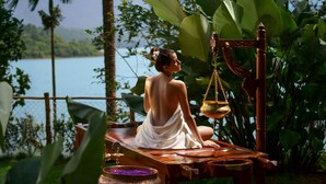 A person sitting on a wooden bench outdoors with a body of water and greenery in the background. - Taj Wayanad Resort & Spa, Kerala (Vythiri)