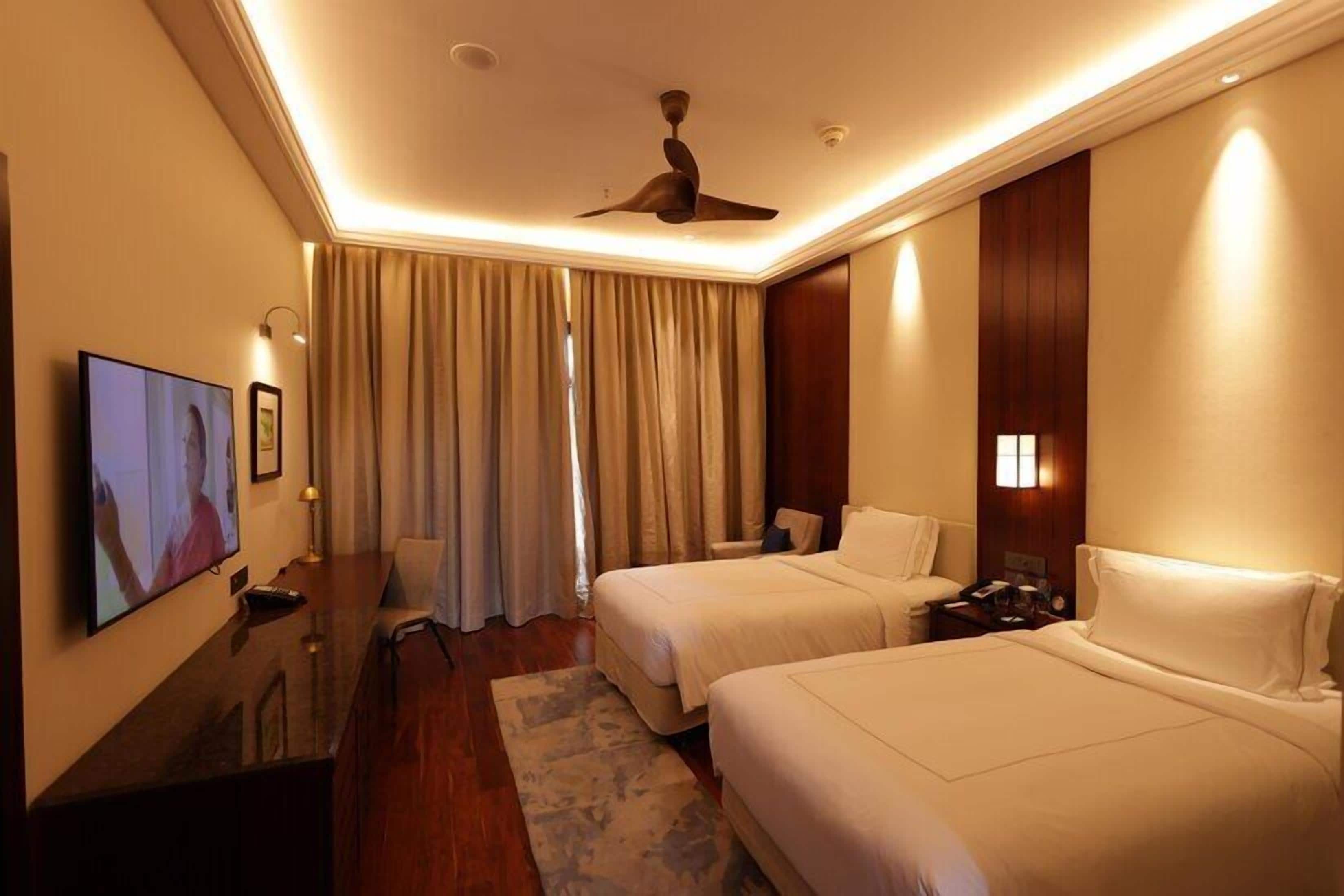 A hotel room with two beds, a TV, a desk, and a ceiling fan.