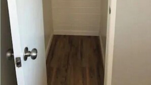 Un couloir étroit doté d’un plancher en bois, d’une porte blanche avec une poignée argentée et d’un mur recouvert de carreaux blancs.