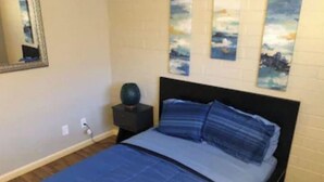 Une chambre à coucher comprenant un lit, une table de chevet, un miroir fixé au mur et trois tableaux verticaux.