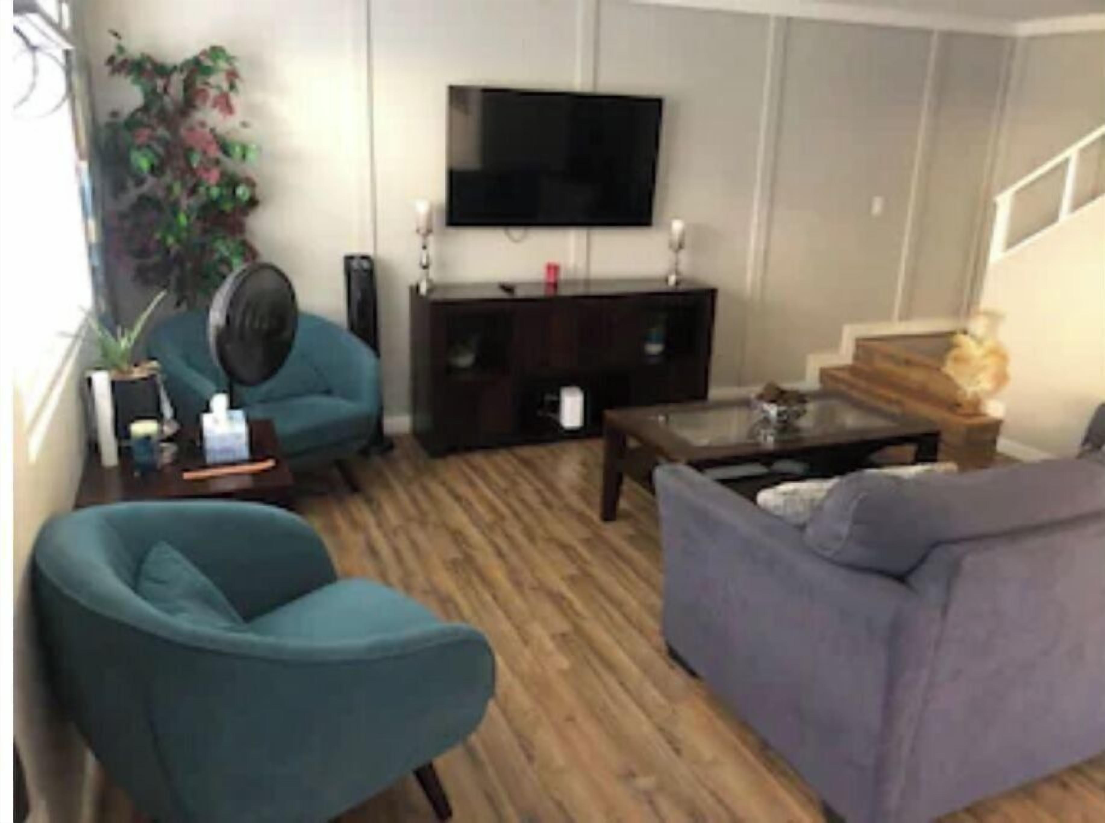 Un salon comprenant un canapé, un fauteuil, une table basse, un téléviseur et un escalier.