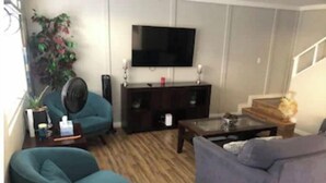 Un salon comprenant un canapé, un fauteuil, une table basse, un téléviseur et un escalier.