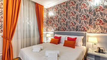 A hotel room with a bed, orange curtains, floral wallpaper, and bedside lamps.