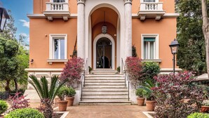 A building with a central entrance, flanked by columns, and surrounded by potted plants. - Mangili Garden Hotel (Rome)
