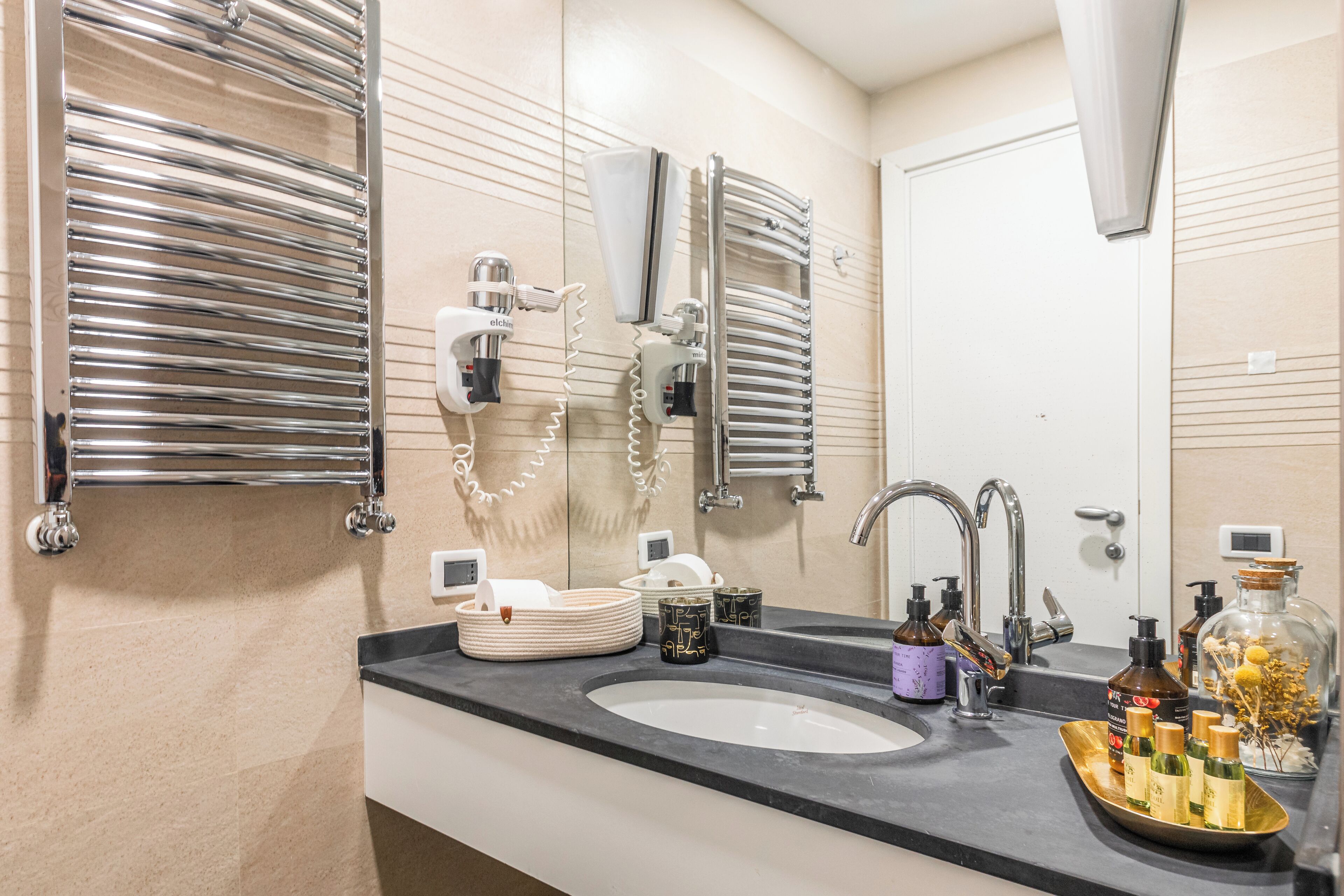 Ett modernt badrum med en stor spegel, kromade handdukshängare, ett handfat med hygienartiklar och en sminkbord.