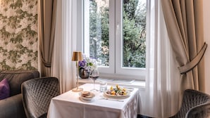 A dining area with a table set for two, a vase with flowers, a wine glass, and a plate of food. - Mangili Garden Hotel (Rome)