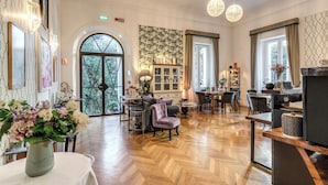 A spacious hotel lobby with a wooden herringbone floor, a seating area with a sofa and chairs, a dining area with a table and chairs, and a reception desk. - Mangili Garden Hotel (Rome)