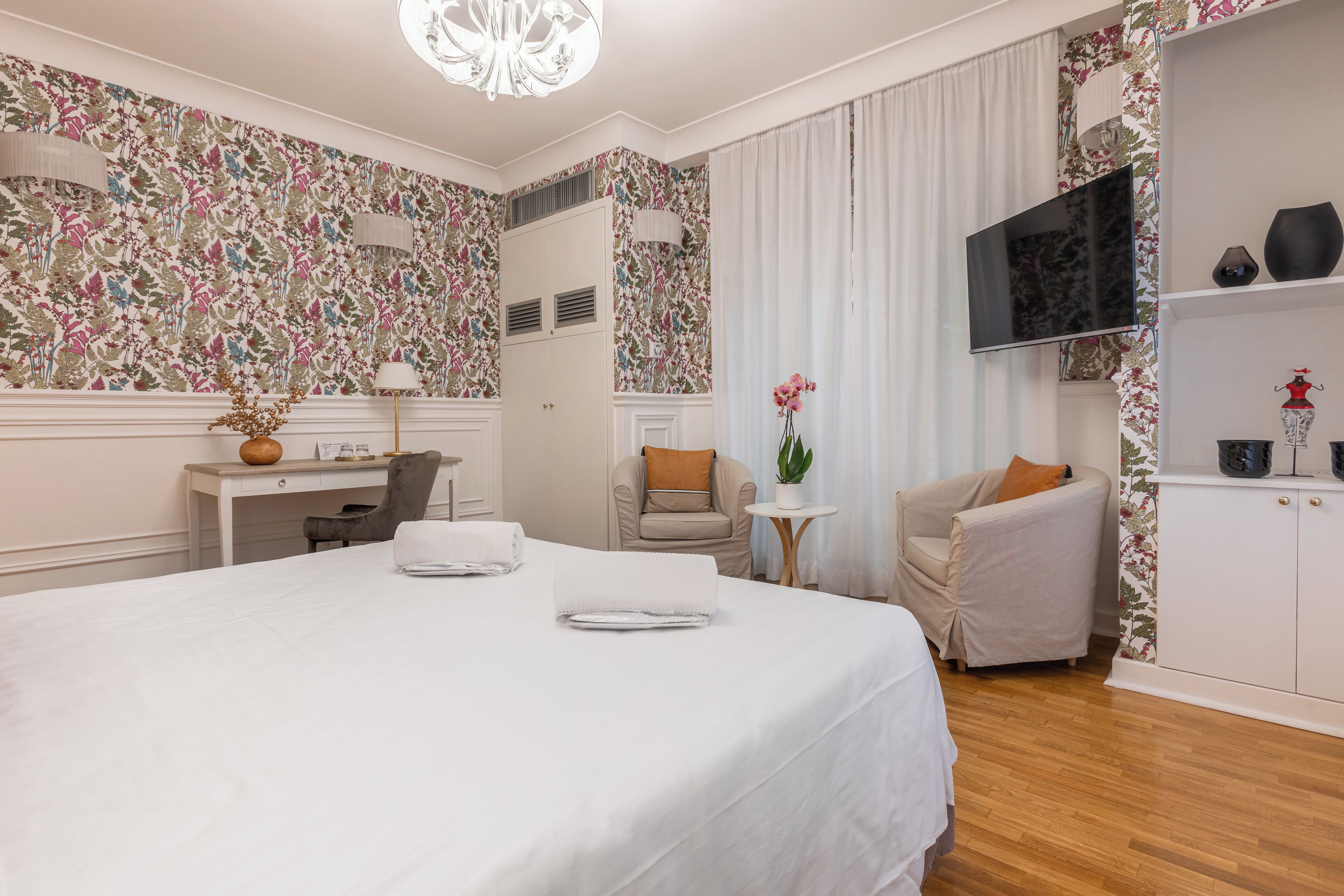 A hotel room with a large bed, a desk, a chair, a TV, and a wardrobe.