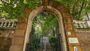 A stone staircase leading up to a gated entrance, surrounded by greenery and a brick wall. - Mangili Garden Hotel (Rome)