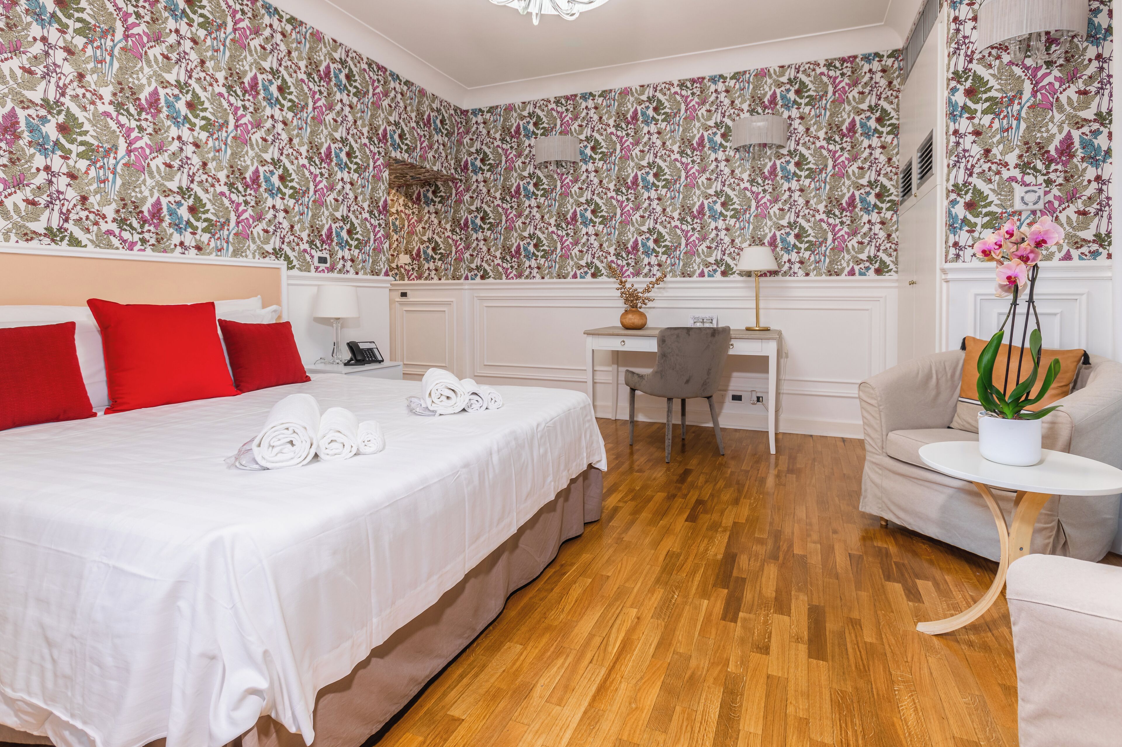 A hotel room with a bed, desk, chair, and a small table with a plant.