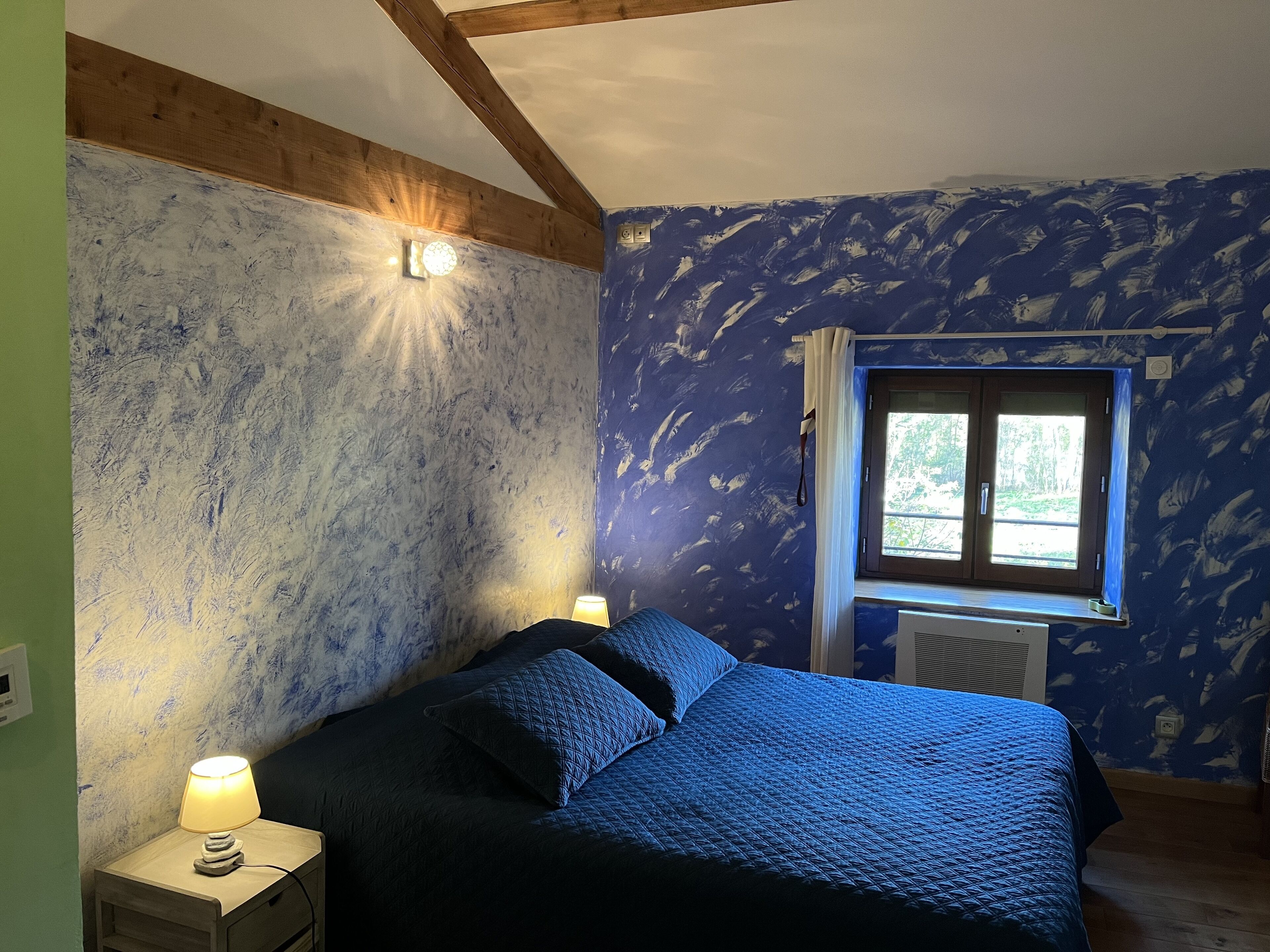 A bedroom with a bed, a nightstand, a window, and a wall with a textured pattern.