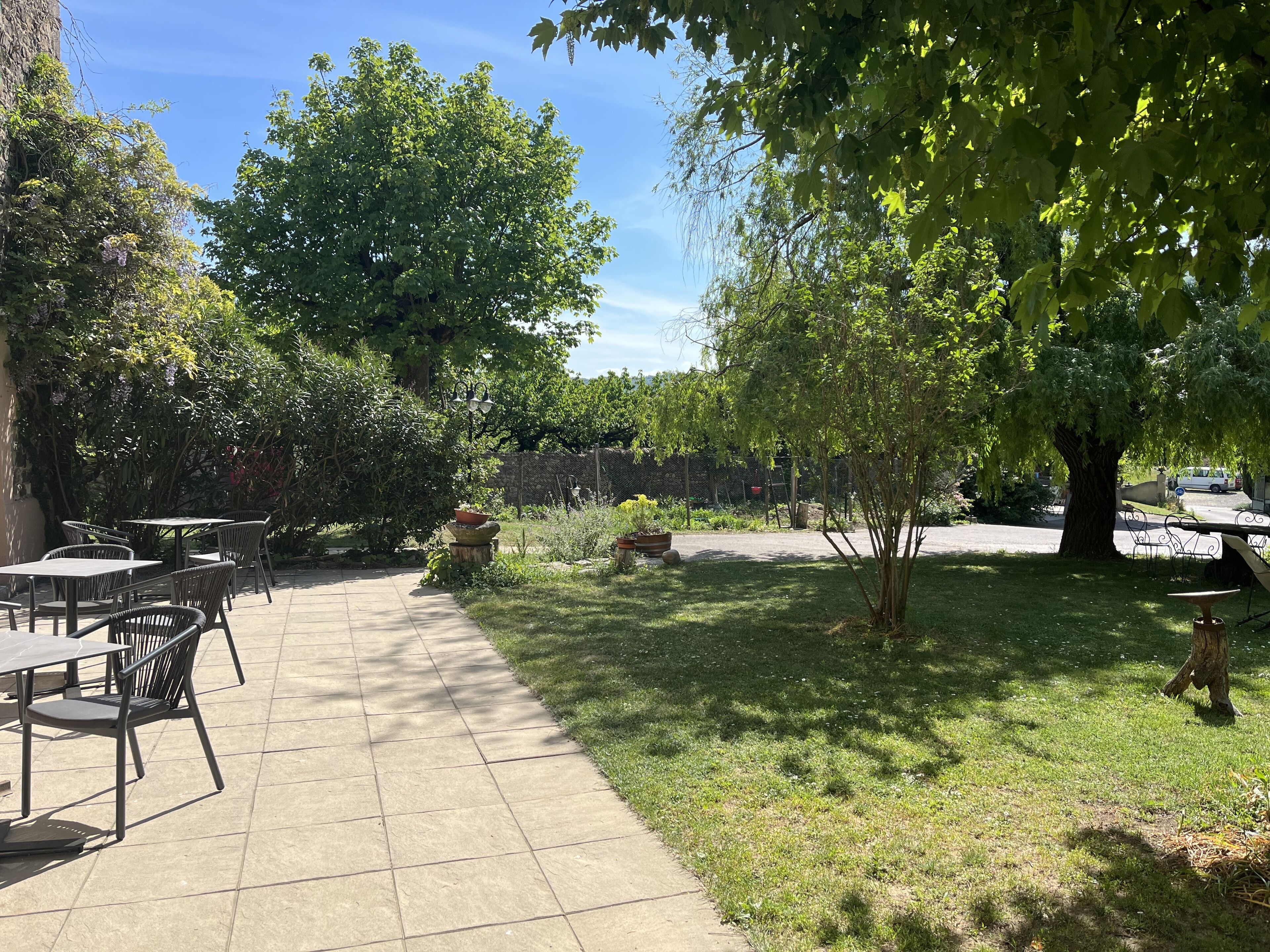An outdoor patio with tables and chairs, surrounded by trees and greenery.