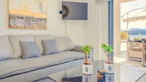 Un salon moderne avec un canapé gris, un téléviseur à écran plat et deux plantes en pot posées sur une table basse en verre.