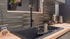 Une cuisine moderne avec un évier noir, une bouilloire en acier inoxydable et une plante en pot posée sur le rebord de la fenêtre.