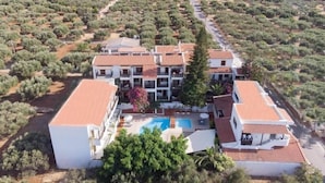 Un hôtel à plusieurs étages doté d’une piscine, entouré d’oliveraies et adossé à un paysage montagneux.