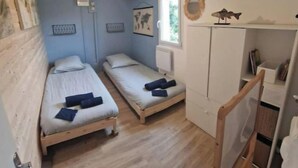A small, cozy room with two single beds, a wooden wardrobe, a small window, and a radiator. - Small cottage (Tourville-sur-Sienne)