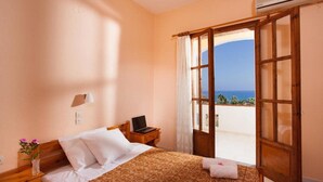 A bedroom with a bed, a laptop on a nightstand, a vase with flowers, and a view of the sea through an open door. - Babis Hotel (Rethymno)