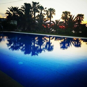 A swimming pool with reflections of palm trees and a sunset. - Babis Hotel (Rethymno)
