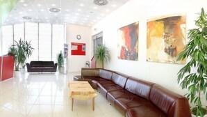 A spacious lobby with a reception desk, a sofa, a coffee table, and several potted plants. - Olympik Artemis Hotel (Prague)