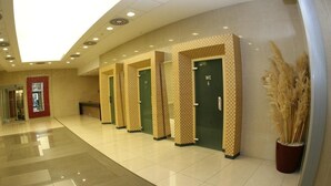 A hotel lobby with a row of green doors labeled "WC" and a potted plant. - Olympik Artemis Hotel (Prague)