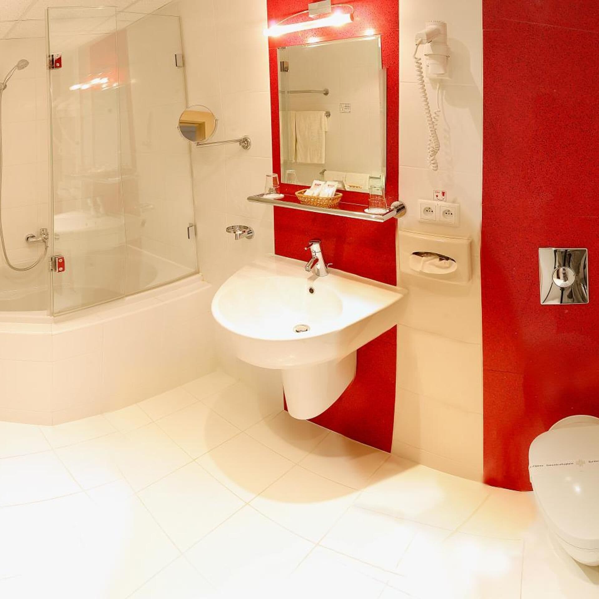 Un baño con cabina de ducha de vidrio, un lavabo blanco, un espejo y una pared de acento roja.