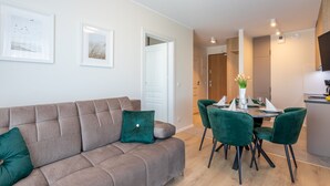 Ett modernt vardagsrum med en soffa, gröna fåtöljer och ett matbord med plats för fyra personer.