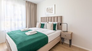 Ett modernt hotellrum med en stor säng, ett nattduksbord och ett fönster med gardiner.