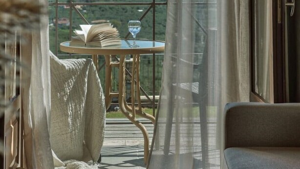 Un balcon donnant sur un paysage montagneux, une table avec un livre et un verre, et un canapé avec un coussin.