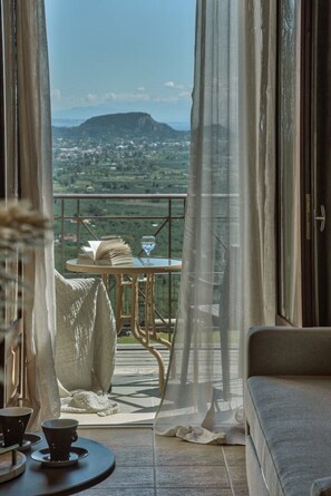 A balcony with a view of a mountainous landscape, a table with a book and a glass, and a sofa with a cushion.